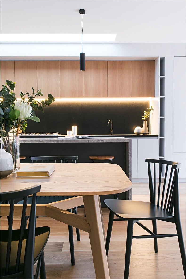 Timber and black dining setting with warmly lit kitchen