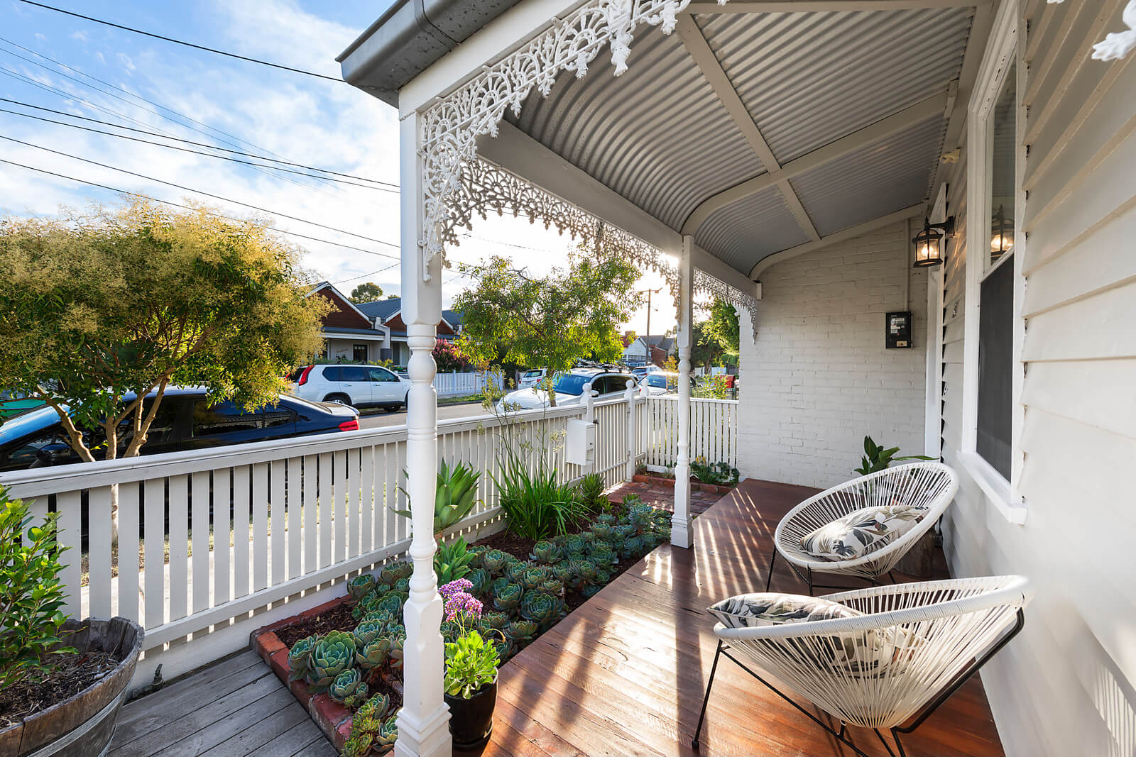 View from the timber deck of a white timber workers cottage, looking out to the succulent garden, white timber fence and Northcote street. White alcapulco chairs.