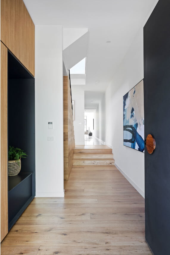 A generous entryway with a feature door painted a deep grey with a large round door handle. Inside is timber flooring, built-in cabinetry details and a large abstract artwork hanging on the wall.