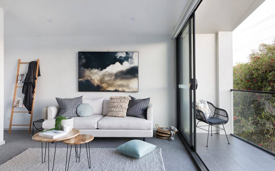 Three seat sofa with a selection of scatter cushions in a variety of different colours and texture. Large centred artwork of a grey, cloudy sky behind sofa.