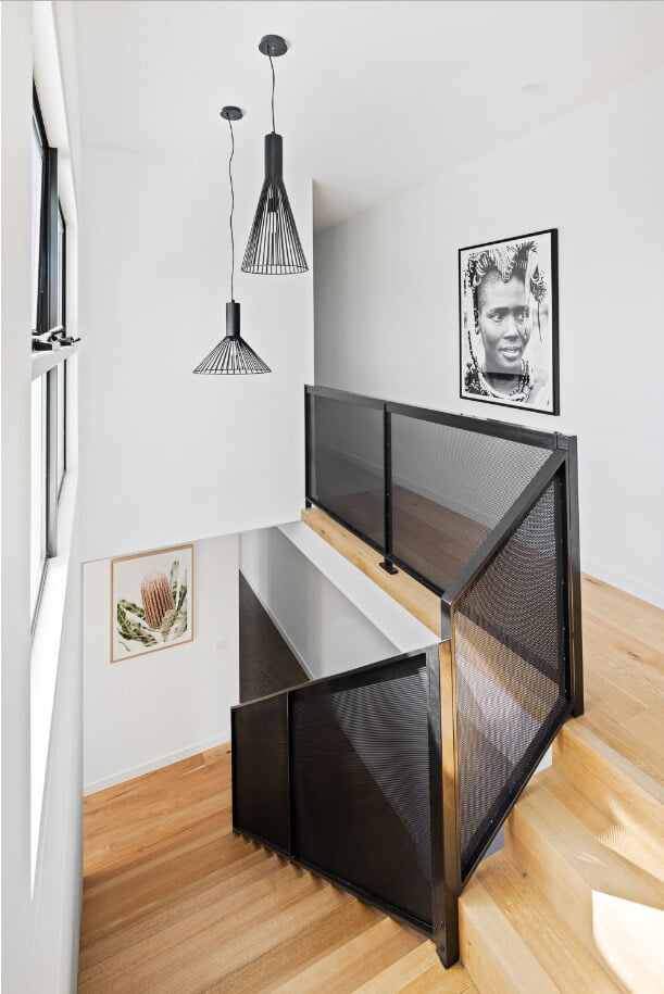 Timber stairs with black perforated metal balustrade. Black modern geometric pendant lighting hanging above stairs and artwork at top and bottom of stairs.