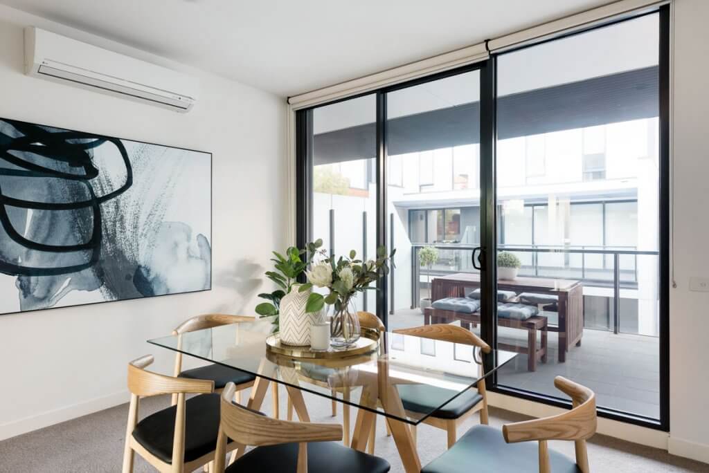 Apartment dining with glass table, timber and leather dining chairs. Glass sliding doors to patio with timber outdoor setting.