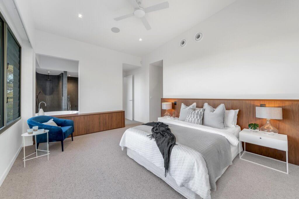 Property styling of a Bardon master bedroom with grey carpet, white walls and feature timber bedhead and built in low set storage.