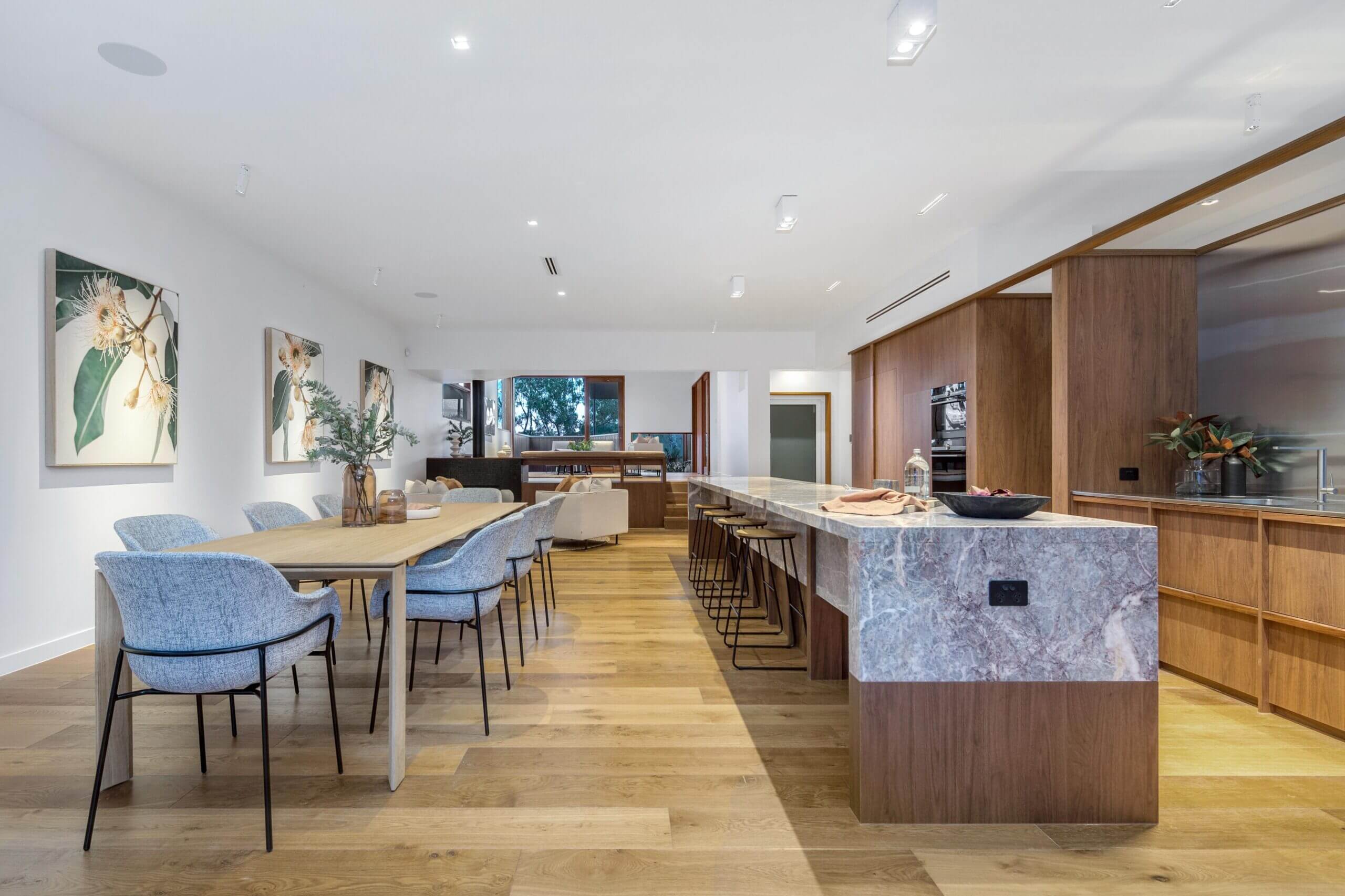 Large kitchen, with marble bench top running parallel to timber dining table with upholstered dining armchairs