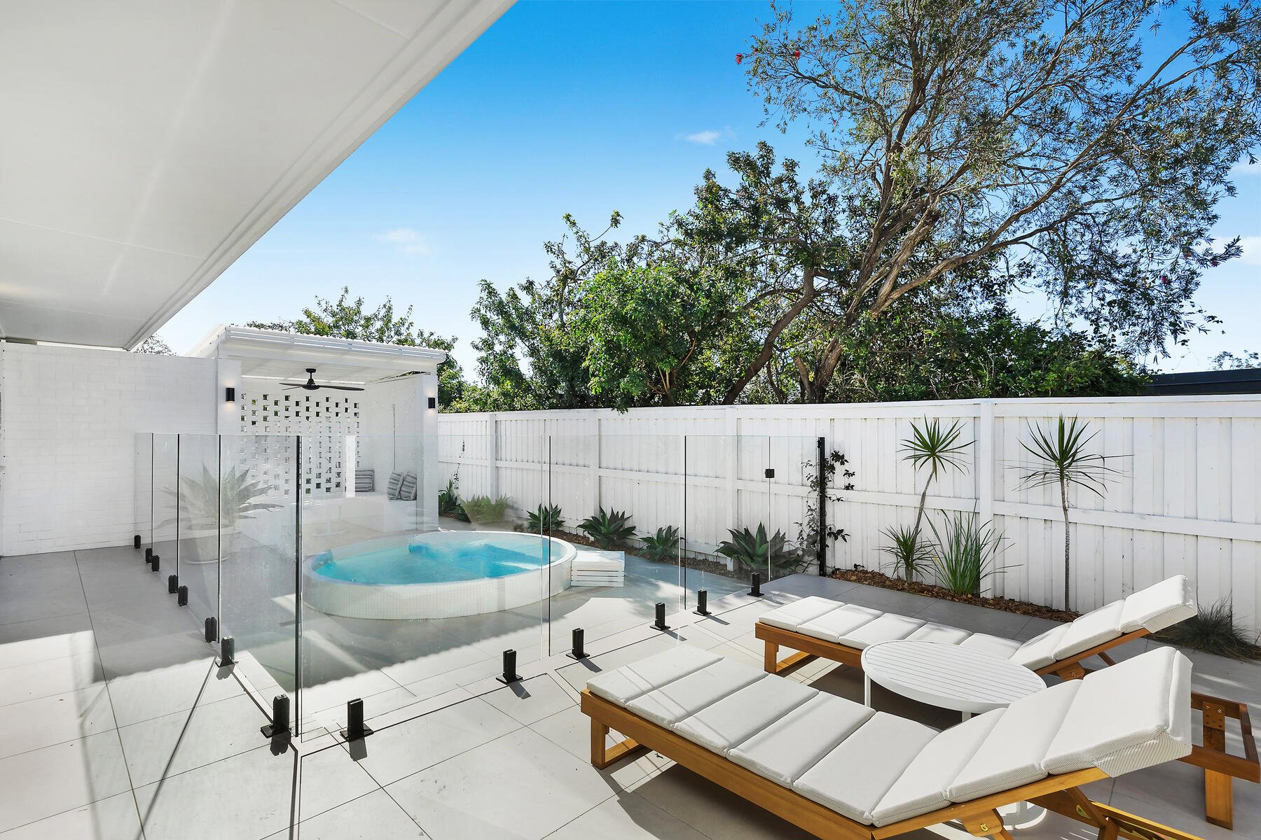 Two sun lounges facing an in ground plunge pool, with white breeze block cabana opposite.